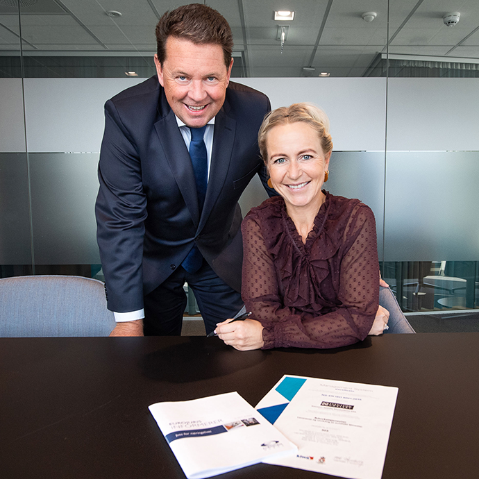 Terje Gundersen og Linda Marie Tanum i Eurojurist Norge smiler til kamera med fignert kontrakt på bordet. Foto.