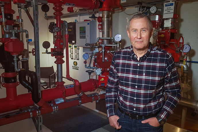 Spesialist i vannbaserte slokkesystemer, Gunnar Sundal, står forran et automatisk slokkesystem. Foto.