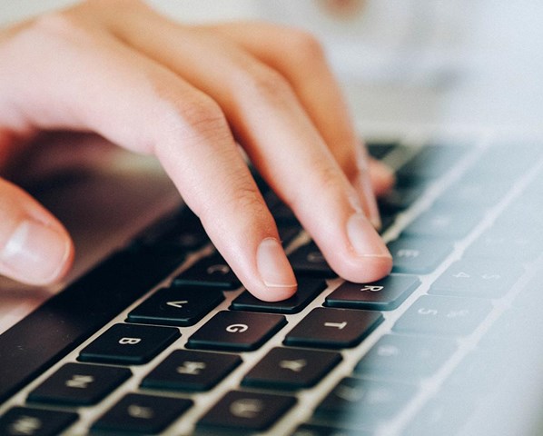 Bilden fokuserar på en hand som skriver på ett tangentbord. 