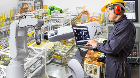 Tekniker kontrollerar robotar med hjälp av dator i tillverkningsindustri. 