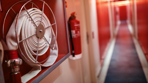Brandsäkerhetsutrustning i en lång korridor, en hoprullad brandslang hänger på väggen bredvid en brandsläckare. 