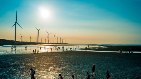 Vindkraft och människor på en strand i solnedgång.
