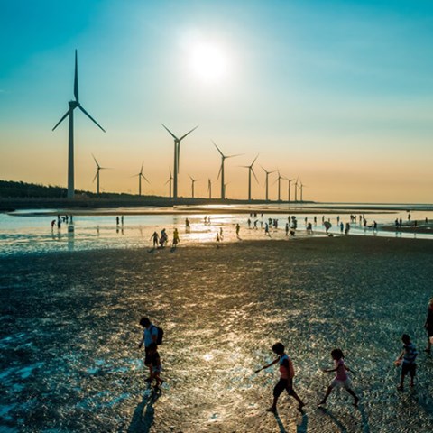 Vindkraft och människor på en strand i solnedgång.