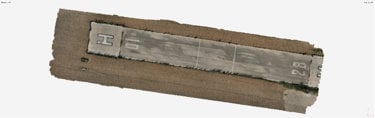 Aerial view of a rectangular concrete helipad with surrounding dirt, featuring helipad markings and faded lines