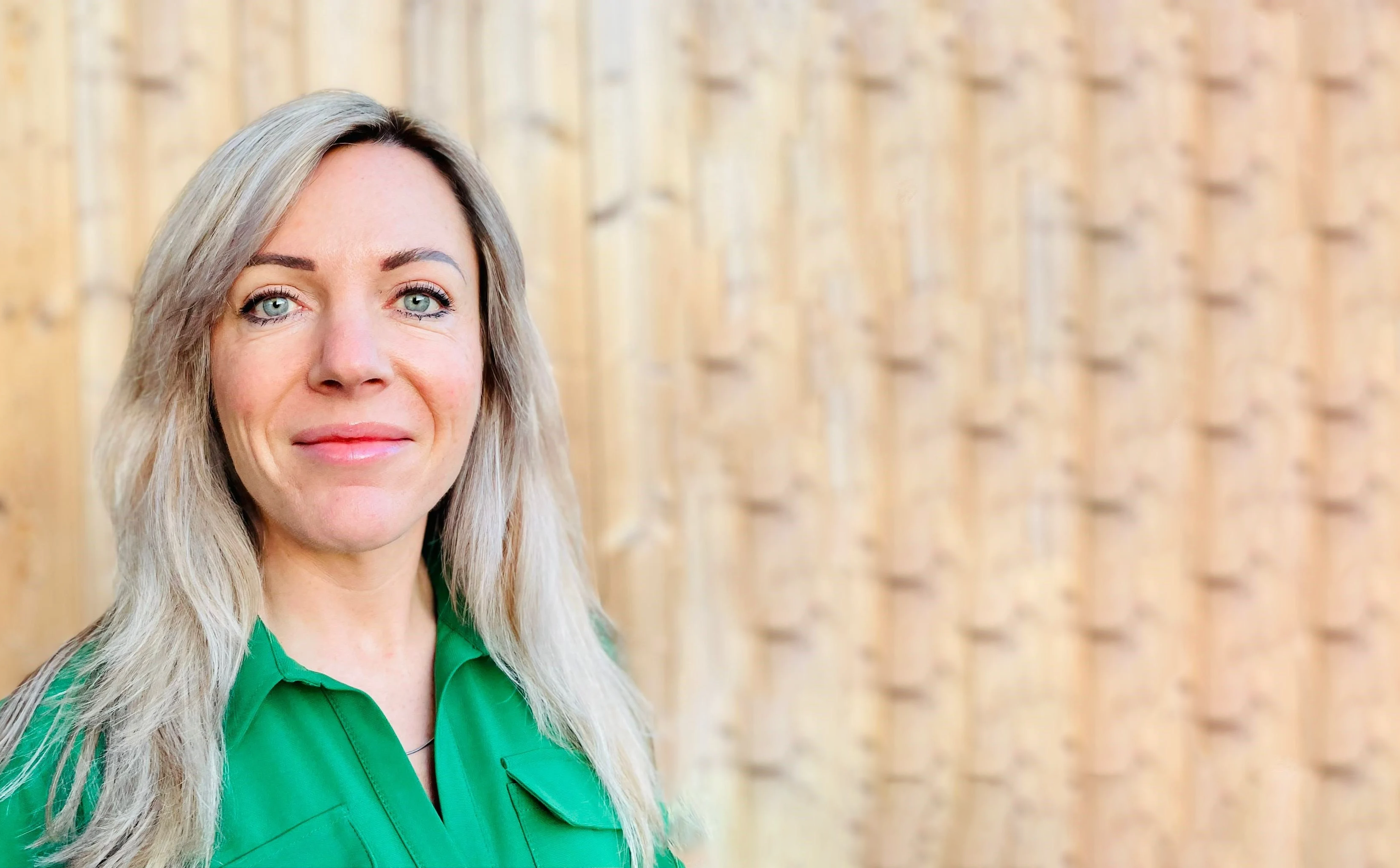 Annelies van Oosterom, International Business Development Manager for Food, Feed, and Agriculture, wearing a green shirt, standing in front of a wooden background
