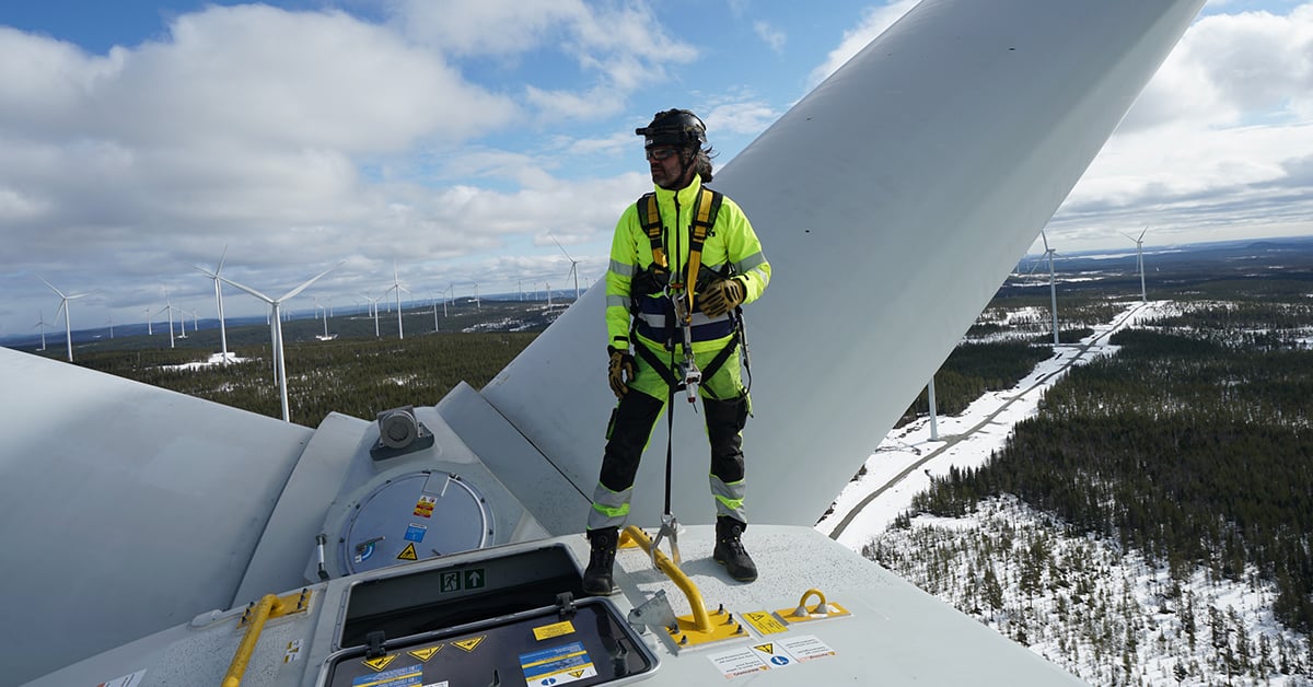 Besiktningsingenjör står längst upp på ett vindkraftverk. 