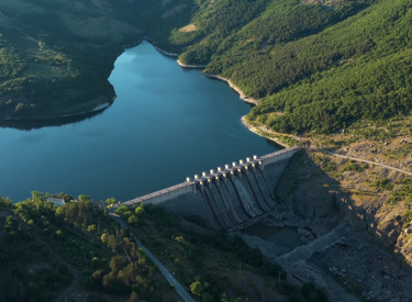 Aerial view of a dam surrounded by lush green hills and a serene river, showcasing a scenic landscape with a reservoir and forested areas