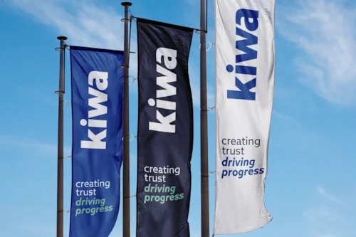 Three vertical flags displaying the Kiwa logo and slogan "creating trust driving progress," set against a background of a blue sky.