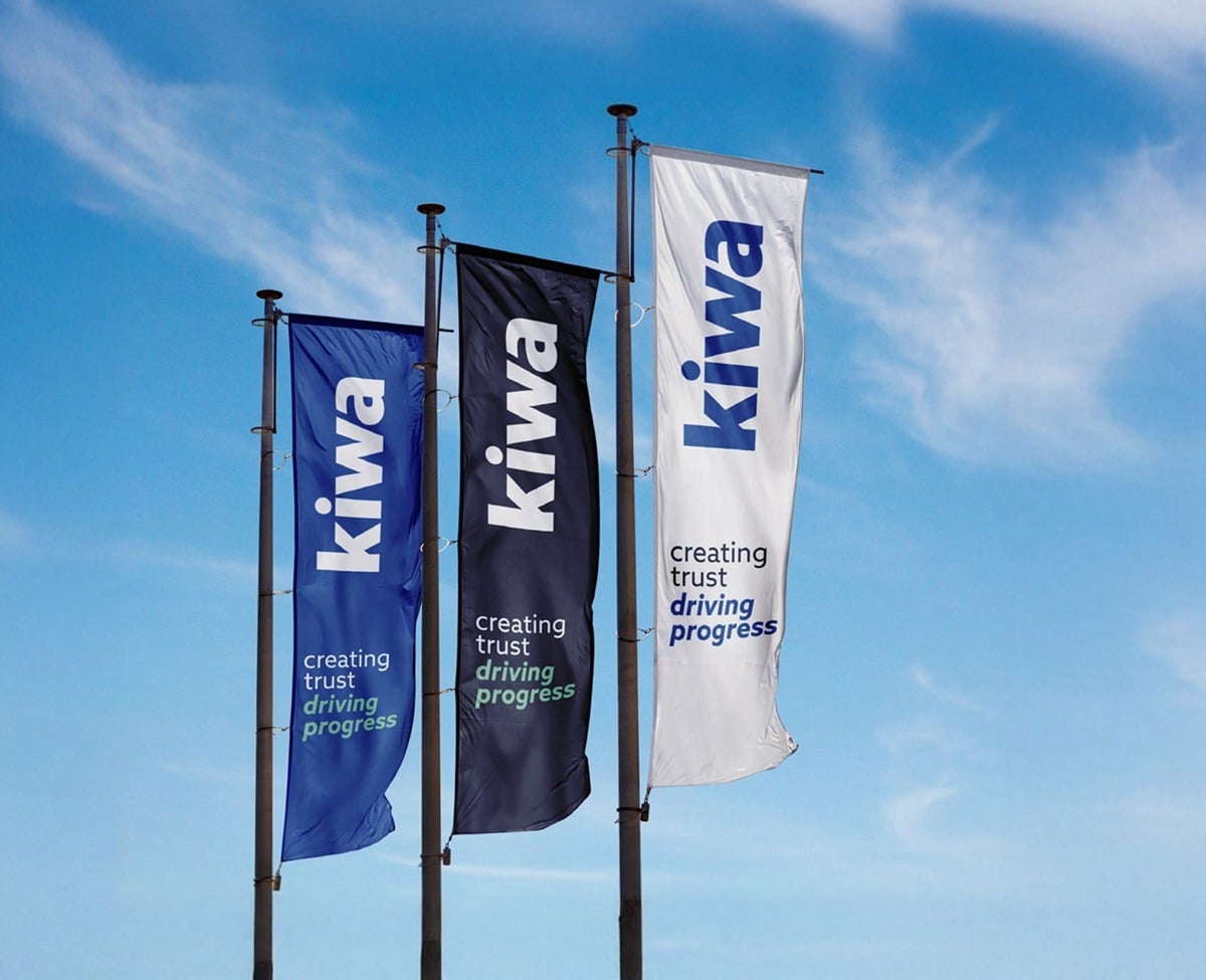 Three vertical Kiwa flags in blue, black, and white against a blue sky, each with the slogan “creating trust driving progress.”