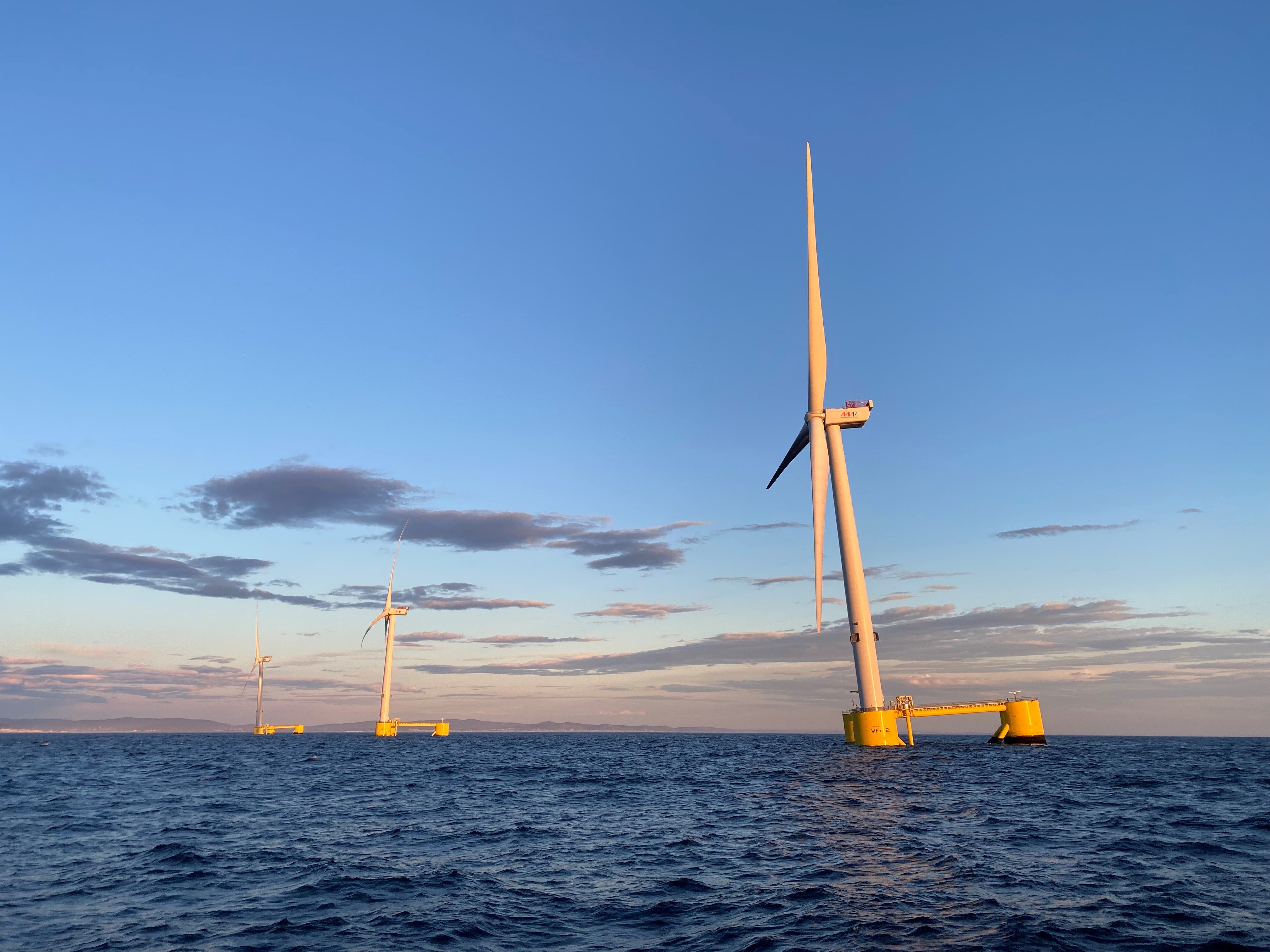 Offshore wind turbines standing in the ocean at sunset under a clear blue sky