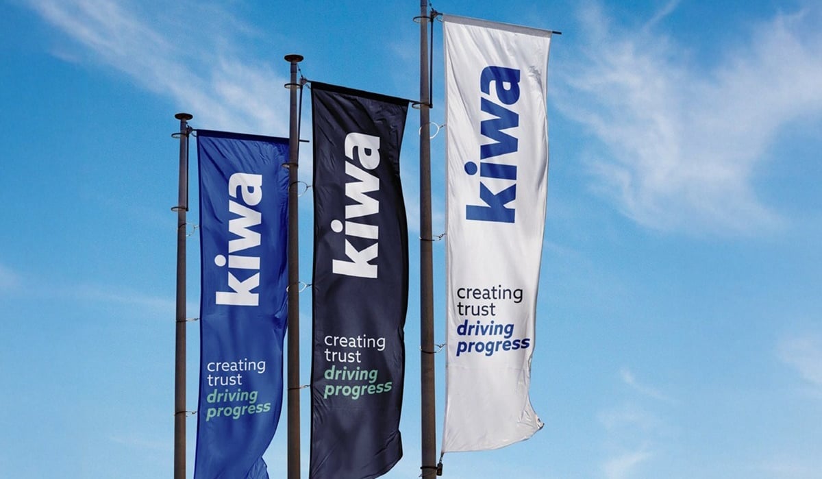 Three vertical Kiwa banners in blue, black, and white against a clear blue sky, each reading “creating trust driving progress.”