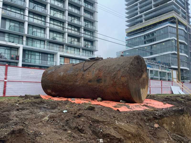 Gros tronc d’arbre coupé posé sur un chantier urbain, devant des immeubles modernes.