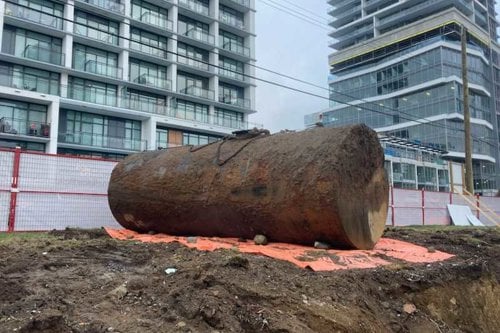 Gros tronc d’arbre coupé posé sur un chantier urbain, devant des immeubles modernes.