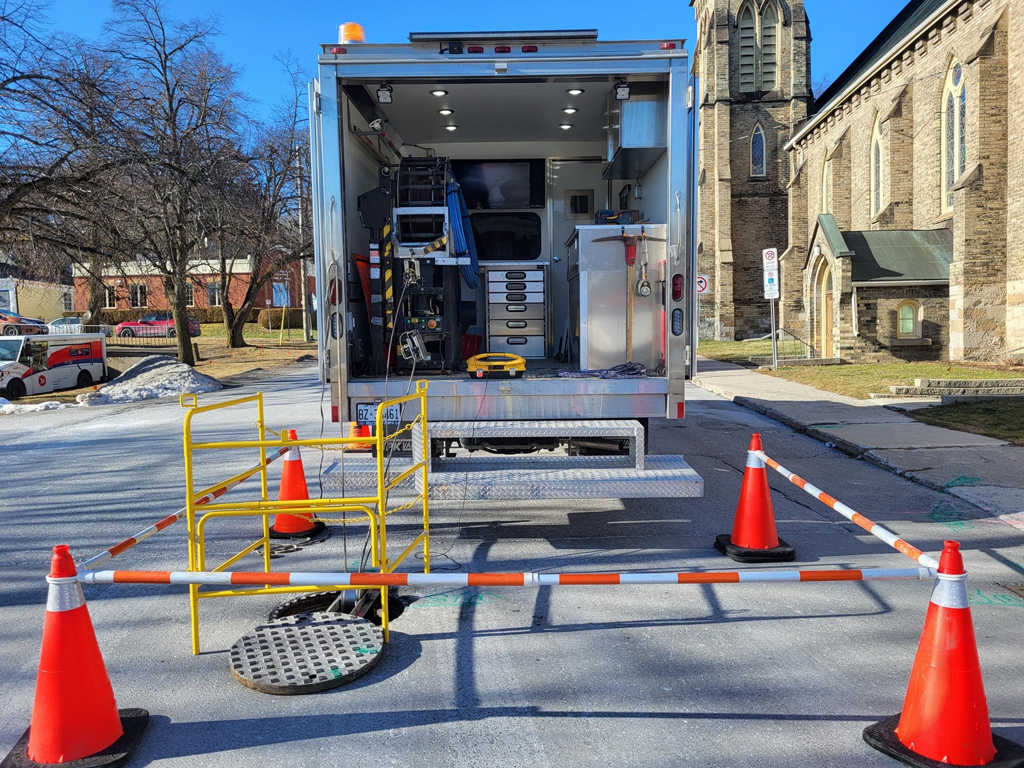 Kiwa T2 camion utilitaire stationné dans une rue, avec cônes de sécurité et barrières autour d’une trappe d’égout ouverte.