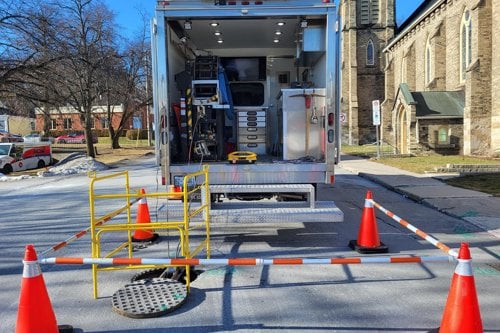Kiwa T2 camion utilitaire stationné dans une rue, avec cônes de sécurité et barrières autour d’une trappe d’égout ouverte.