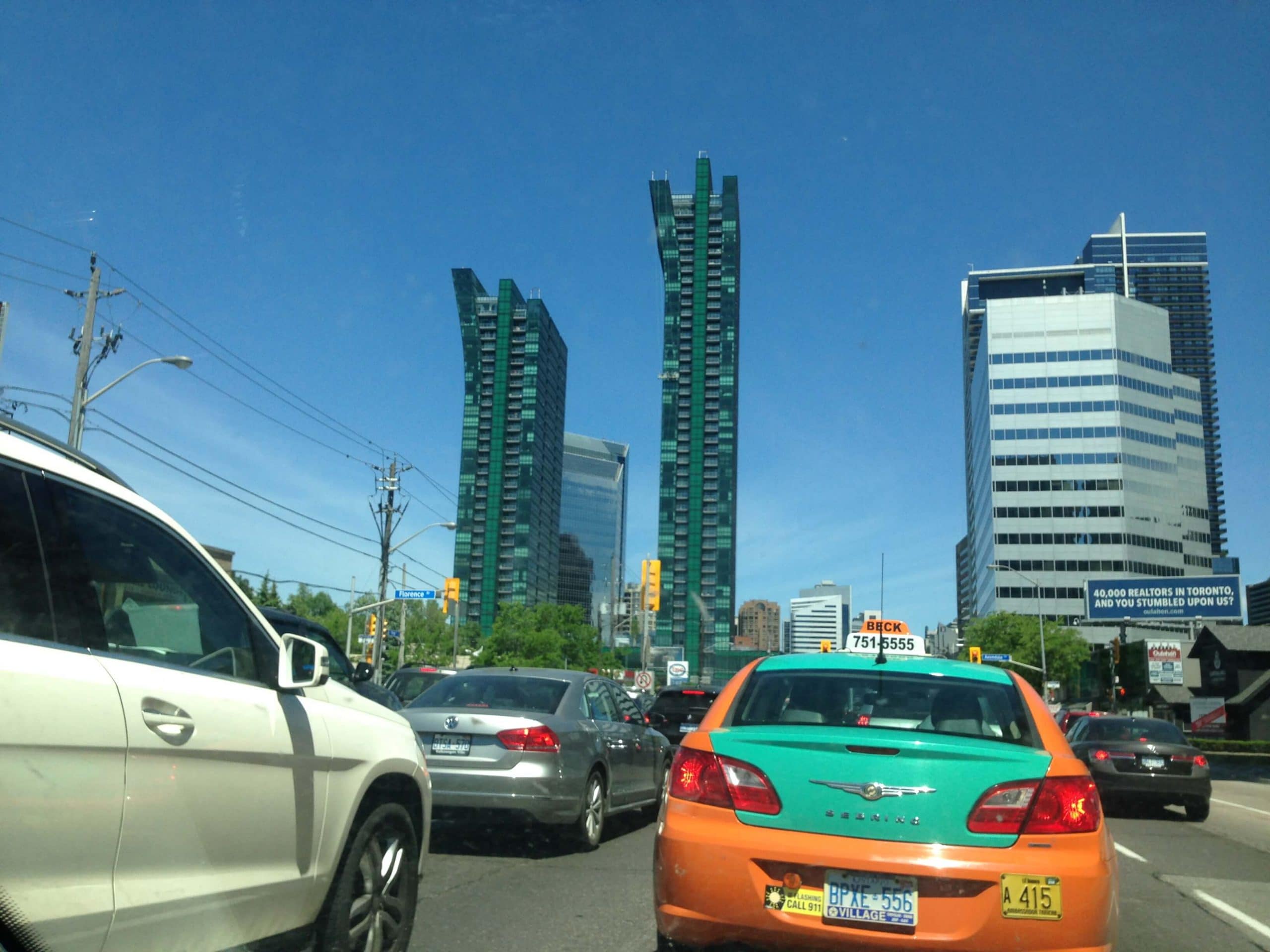 Traffic on a city street with cars in the foreground and the Emerald Tower under a clear blue sky.