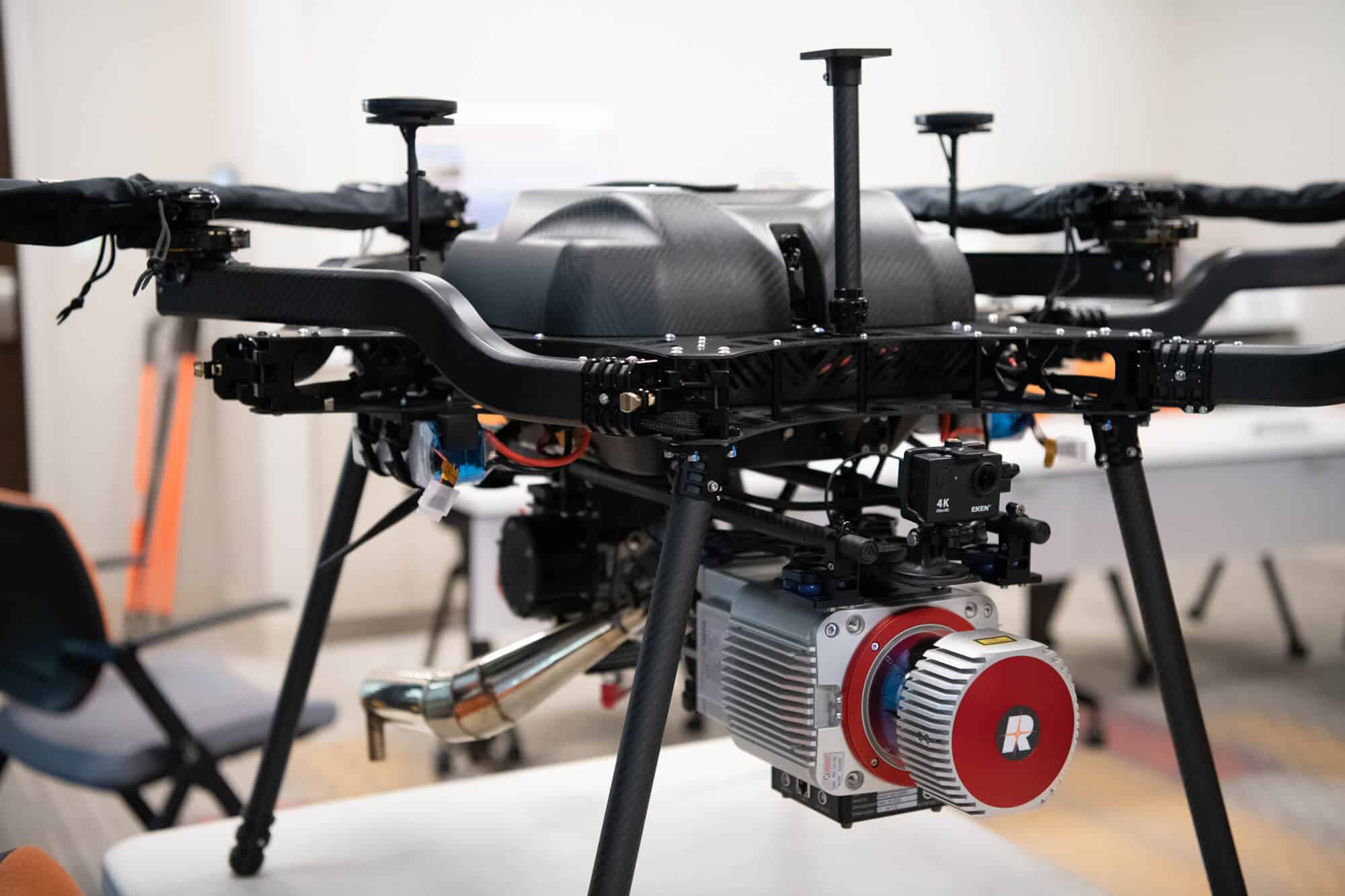 Close-up of a professional quadcopter drone with a mounted 4K camera and large lens in an indoor setting.