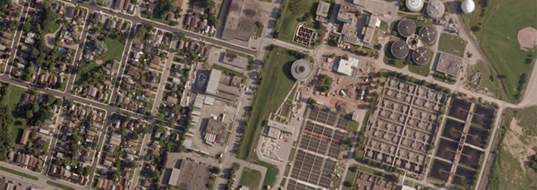 Aerial view of a suburban neighbourhood beside the Hamilton wastewater treatment facility with circular tanks and rectangular settling ponds.