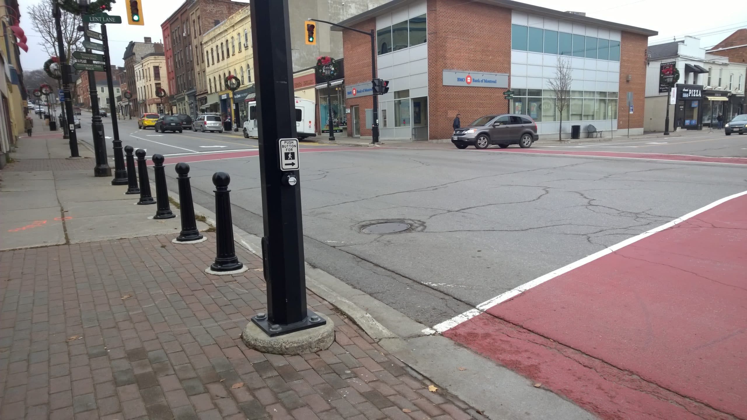 Downtown street intersection at Port Hope with brick sidewalks, black bollards, traffic lights, parked cars, and storefronts on a cloudy day.