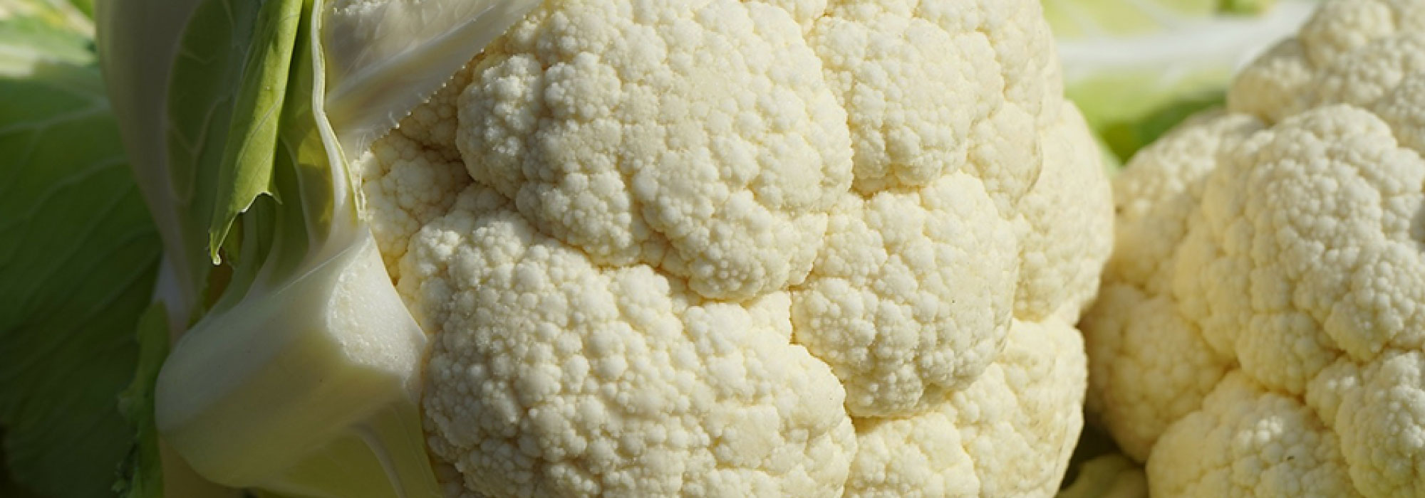 Coliflor fresca con hojas verdes apilada en una superficie de madera.