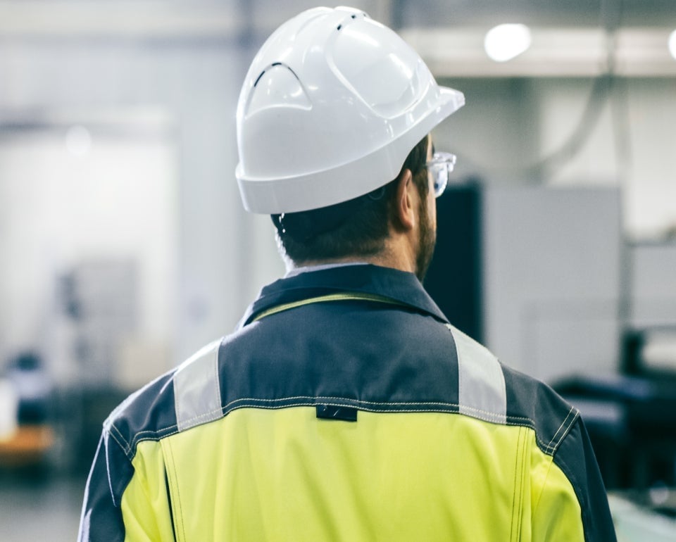 Hombre con casco de seguridad y chaqueta de alta visibilidad en un entorno industrial.