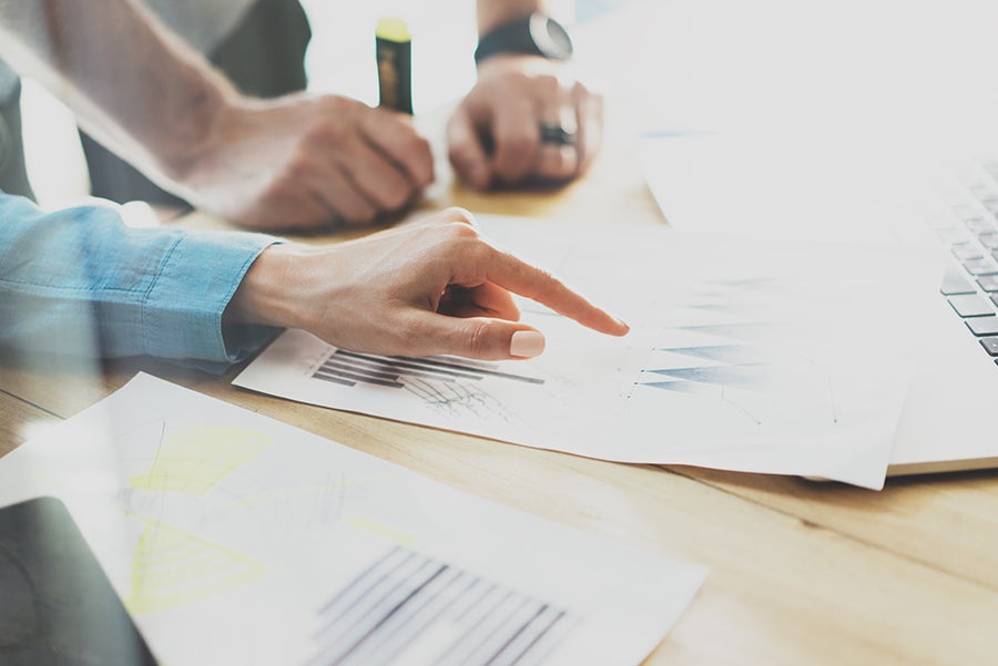 Rankos rodo į spausdintus grafikus ant stalo šalia nešiojamojo kompiuterio – Kiwa vadybos sistemų sertifikavimas, ISO 9001, ISO 14001, ISO 45001, ISO 50001