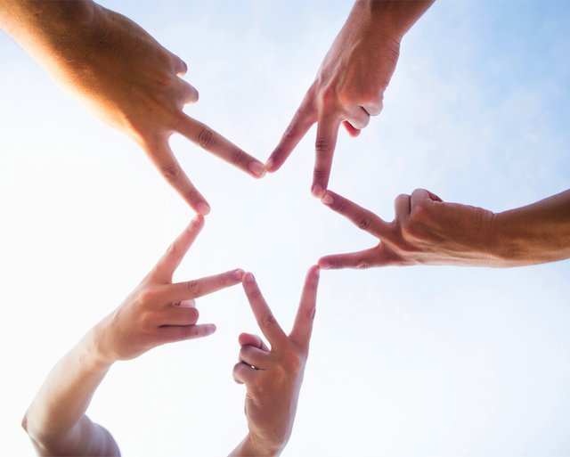 Cilvēku rokas savienotas, veidojot zvaigzdes formu uz zilas debesu fona.