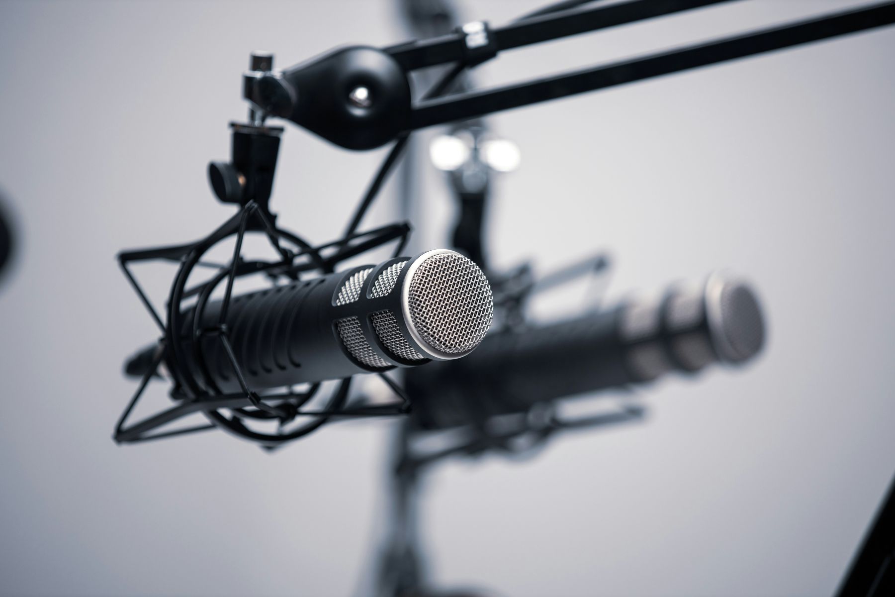 Close-up of a professional microphone with a pop filter on a studio boom arm stand, set against a blurred background.