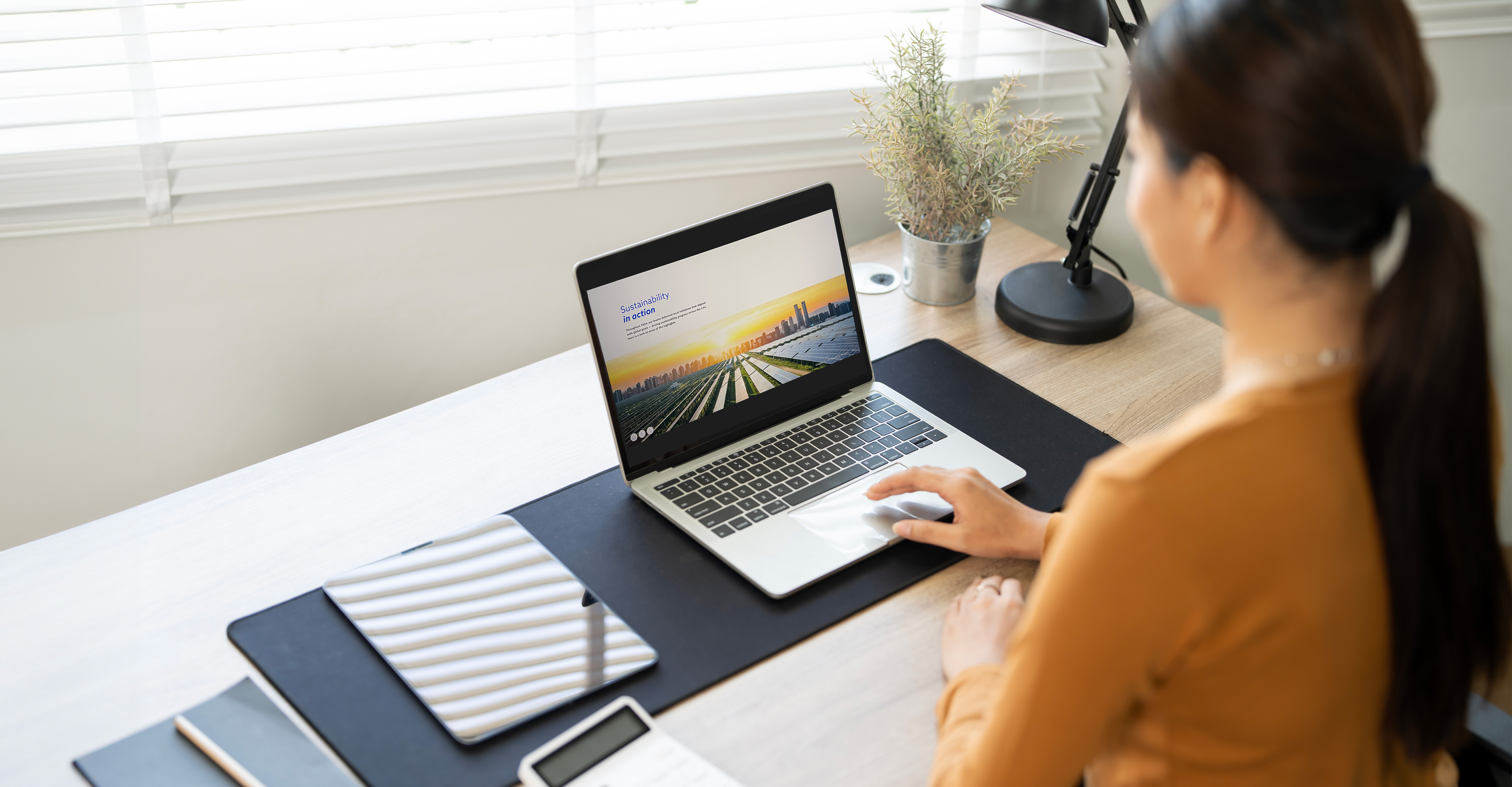 Woman working on a laptop at a desk, displaying a presentation on sustainability featuring a city skyline
