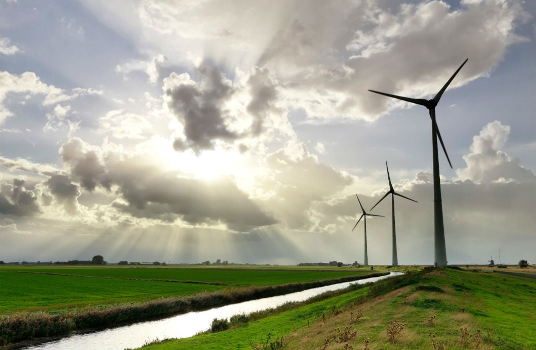 open sunny field with three wind turbines next to a canal