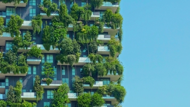 Modern high-rise building with lush vertical gardens and balconies against a clear blue sky