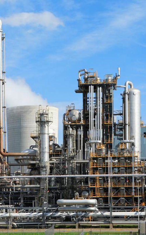 Industrial refinery complex with large silos and smokestacks, against a clear blue sky, showcasing manufacturing and industry