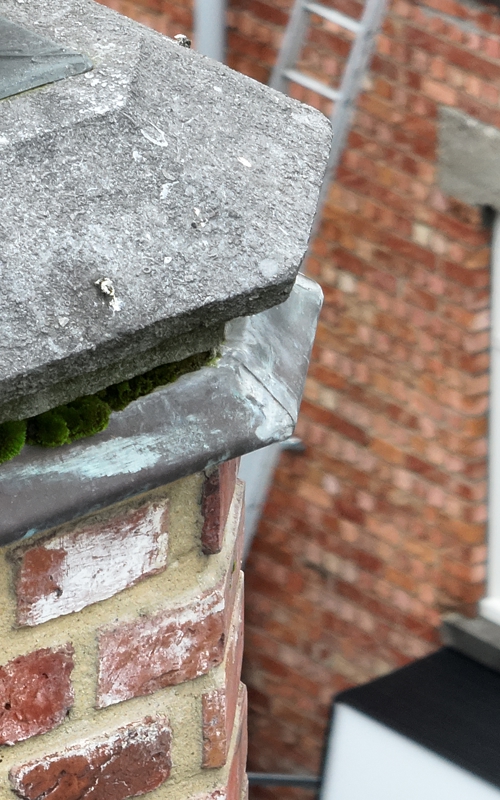 Footage of an old brick chimney with moss growth from a facade inspection, showing building exterior and window in the background, captured from a high angle