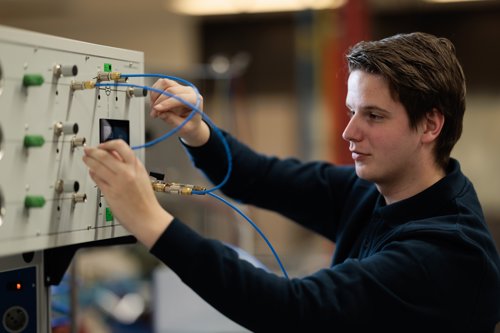 Young man connecting blue cables to an industrial machine in a workshop.