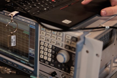 A hand operating a laptop connected to an electronic signal analyzer in a laboratory setting