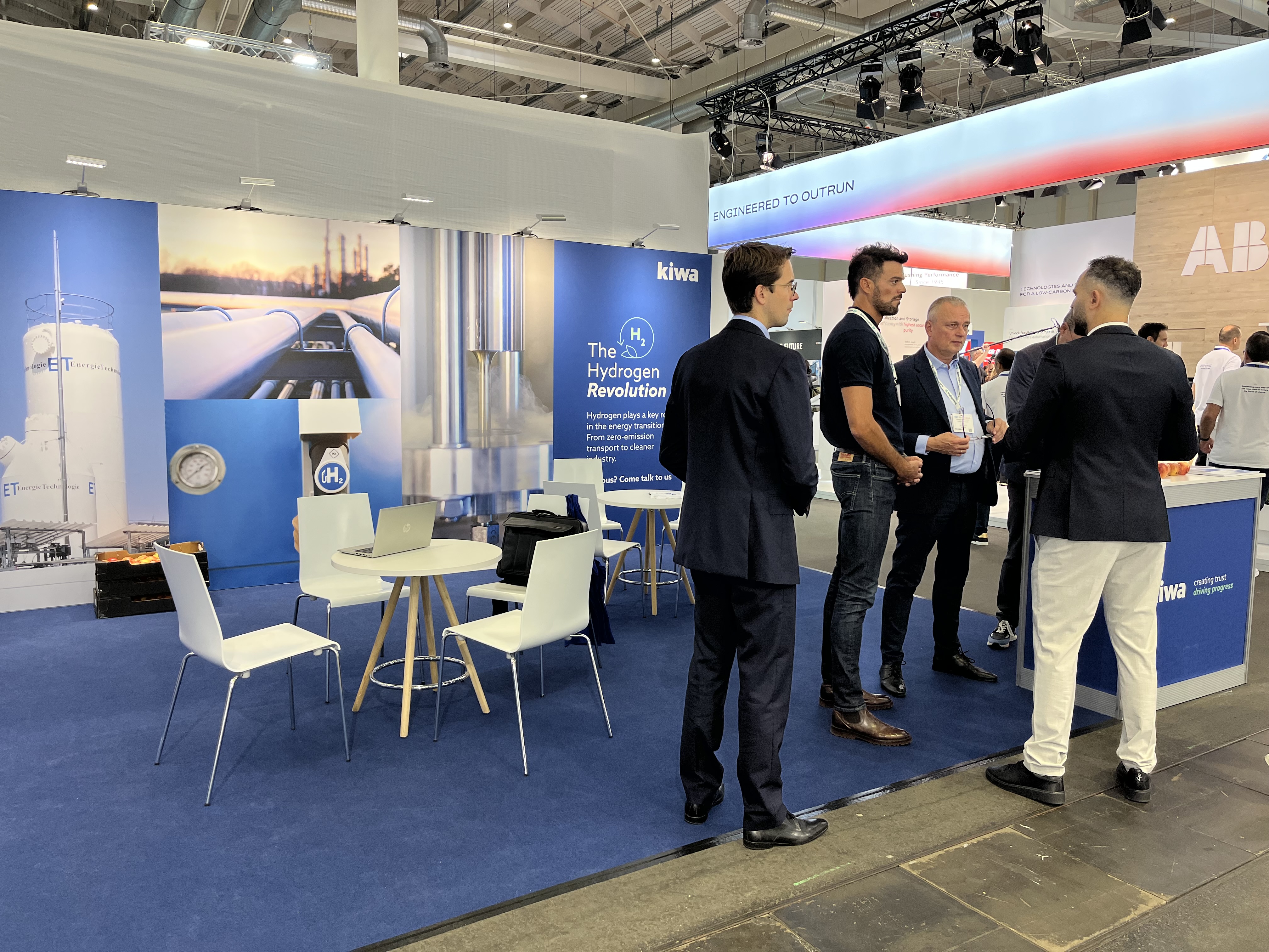 Business professionals talking at a hydrogen energy trade show booth with Kiwa branding and blue exhibition displays