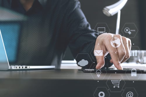 Cilvēks melnā kreklā pieskaras viedtālrunim, apkārt redzamas tehnoloģiju ikonas un biroja vide.