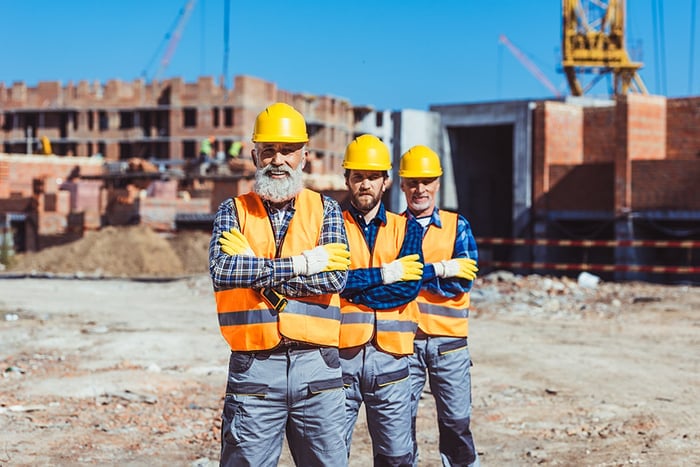 Trys statybininkai su aprangomis statybų aikštelėje
