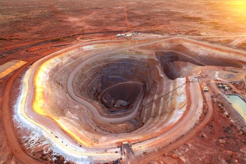 Aerial view of a large open-pit mine at sunset, showing terraced earth layers and surrounding barren landscape in a remote area