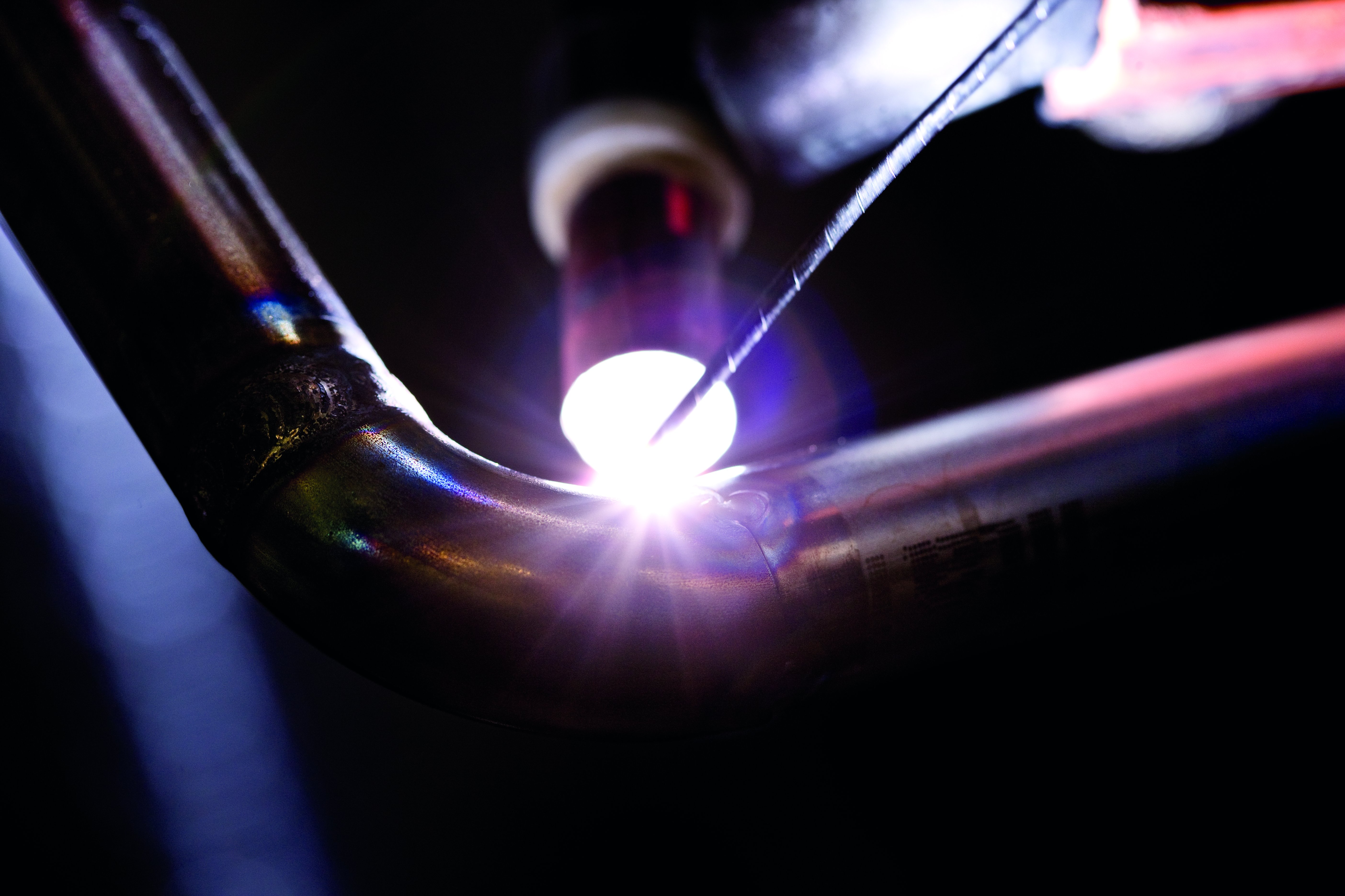 Artimas vaizdas į suvirinimo procesą – suvirinimo degiklis sukuria ryškią šviesą ant metalinio vamzdžio lenkimo vietos – suvirintojų kvalifikacijos tikrinimas ir sertifikavimas pagal LST EN ISO standartus