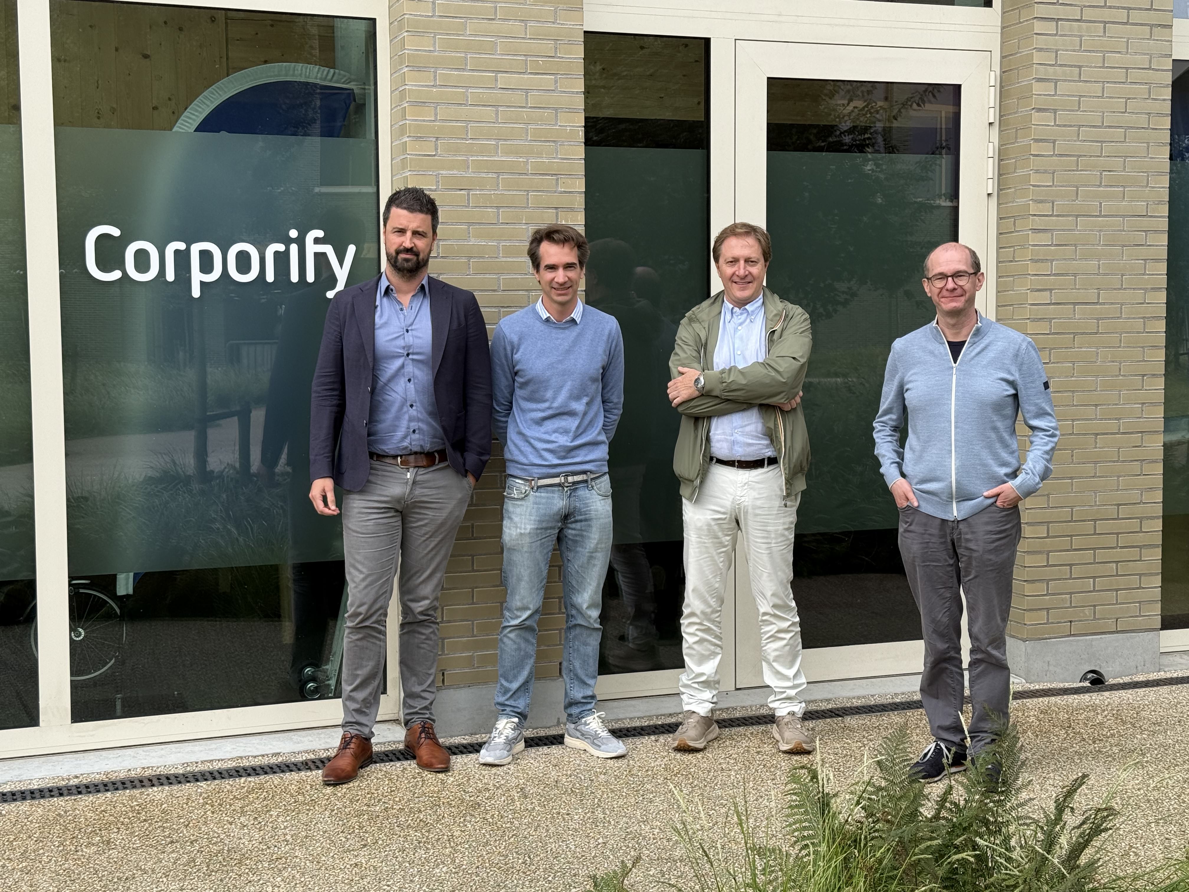Four men standing outside a Corporify office building, with the company name visible on the glass door.