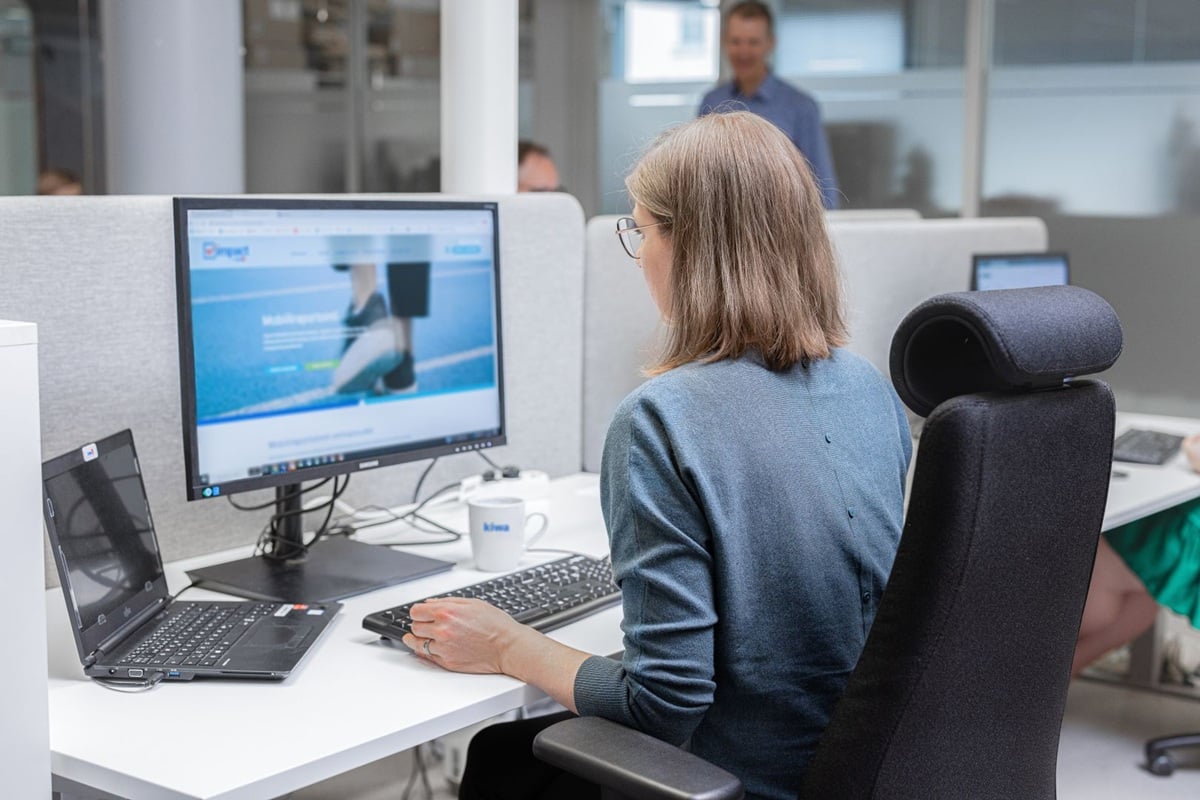 Woman working at a desktop computer in a modern office, using a laptop and keyboard at a workstation.