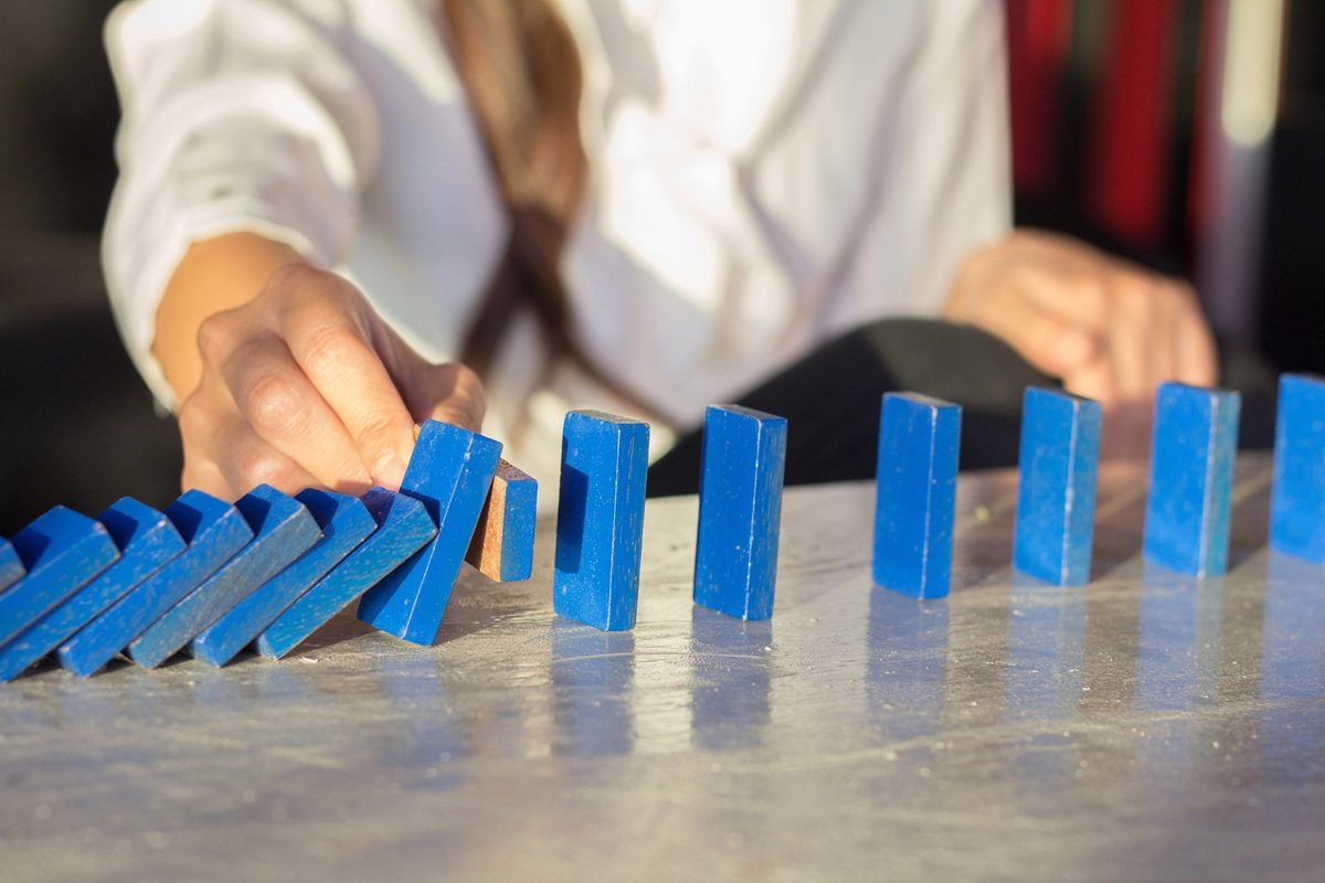 A person in a white shirt is setting up blue dominoes in a row on a table.