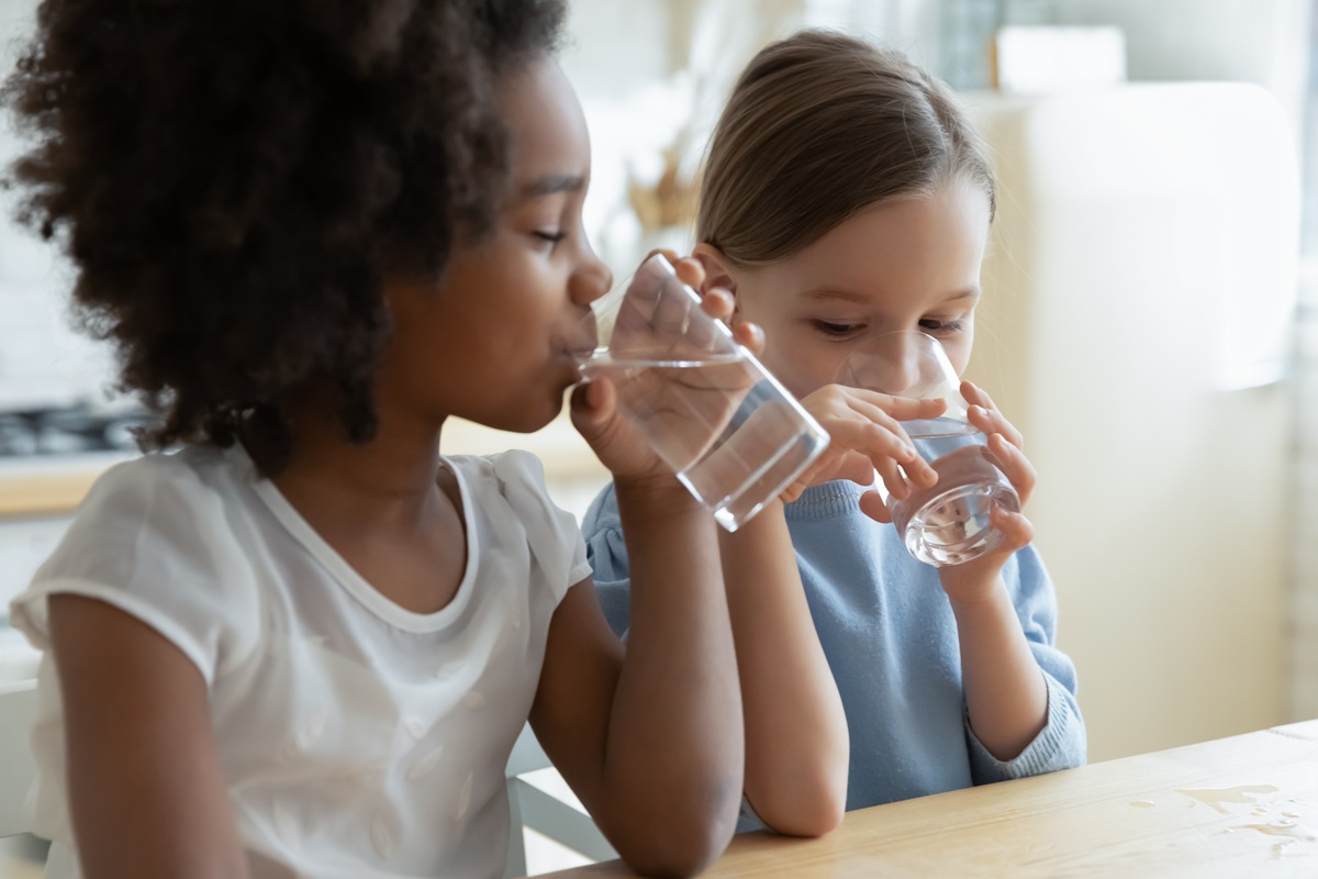 Two children are drinking water at a table in a kitchen