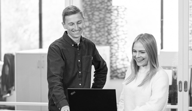 2 medarbeidere hos Kiwa smiler og ser p&aring; en PC skjerm. Bilde