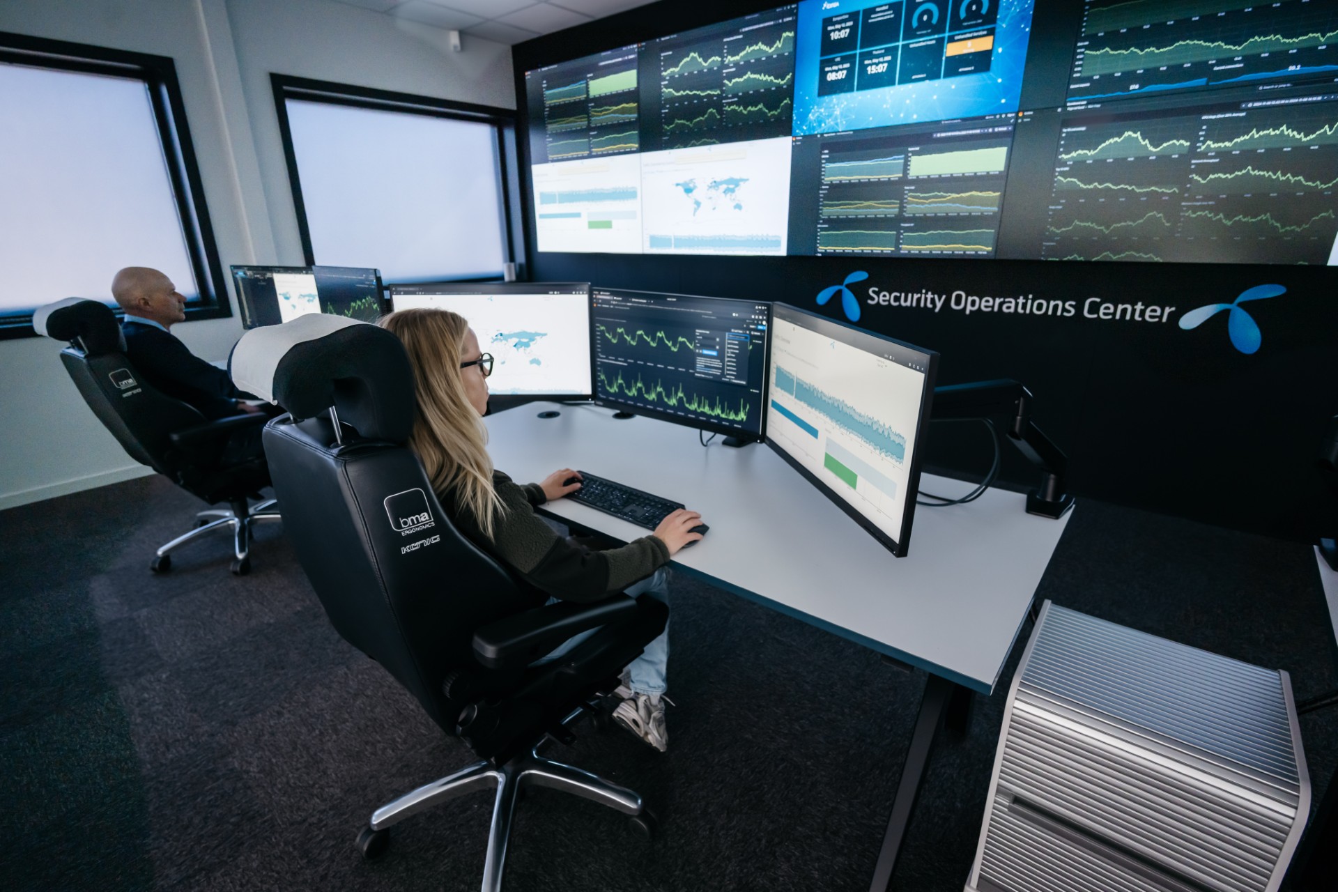 To ansatte i Telenor Cyberdefence sitter foran skjermer og overvåker dataaktivitet i et sikkerhetsoperasjonssenter.