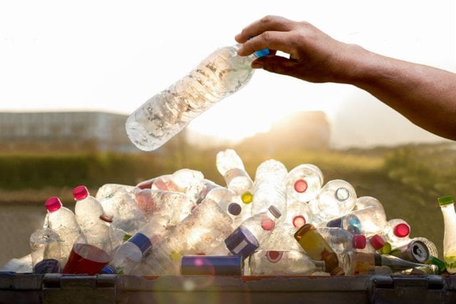Someone places a plastic bottle onto a pile of empty bottles ready for recycling