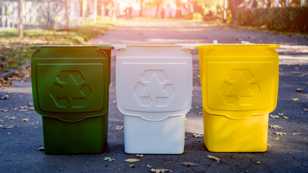 Green, white and yellow recycling bins stand in a row on an outdoor pathway