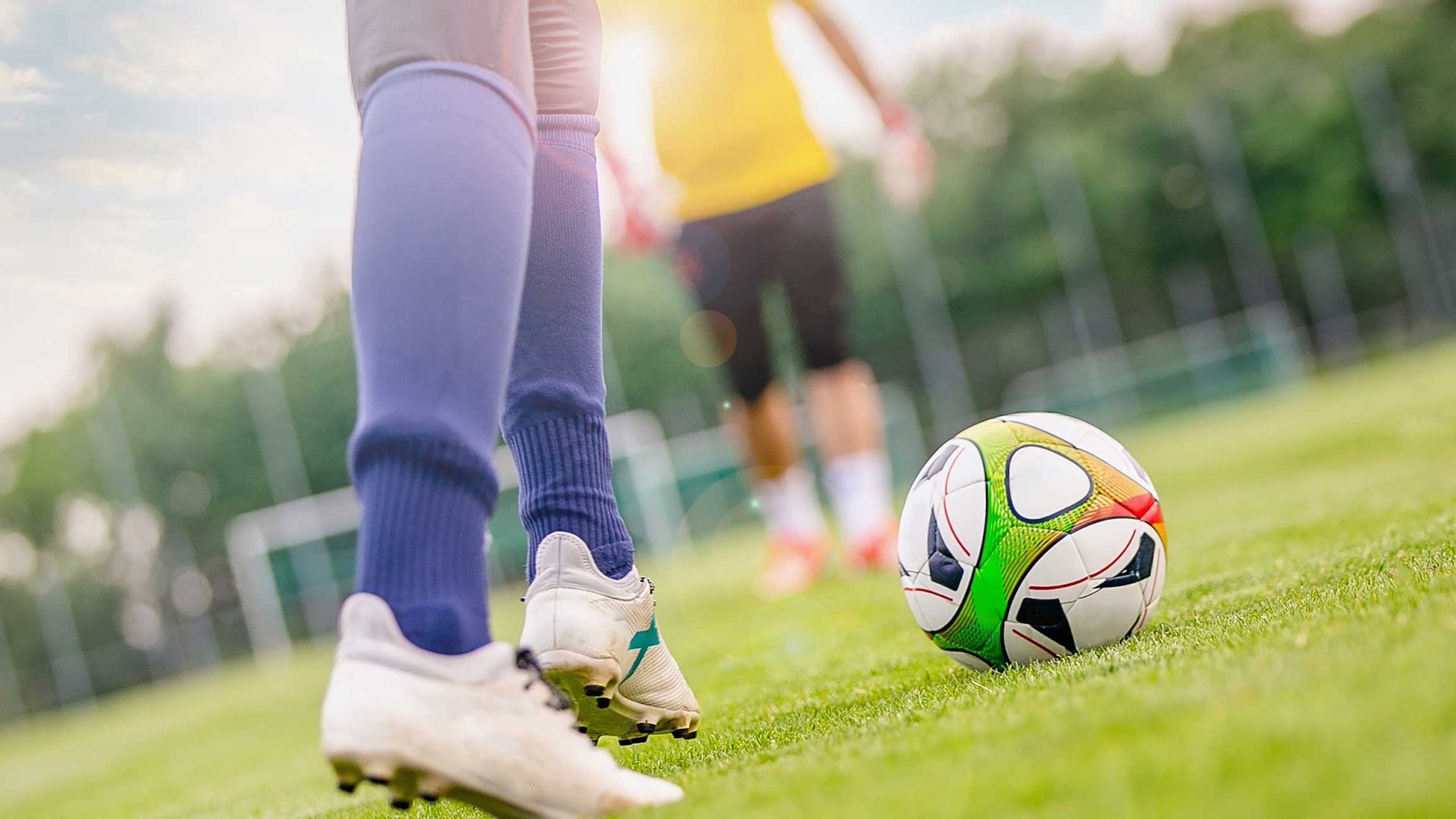 Person som spelar fotboll på en gräsplan, med fokus på fötter och en fotboll nära.