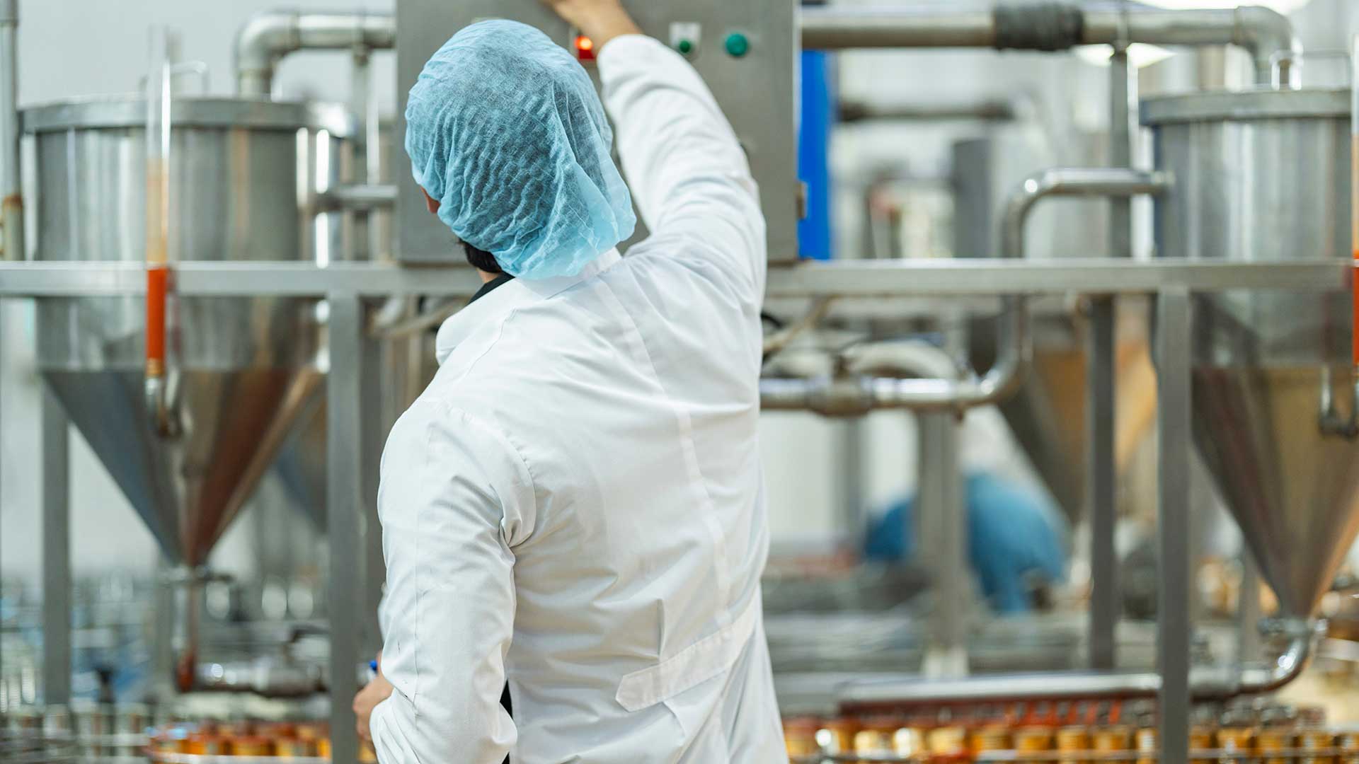 Person i vit skyddsklädsel kontrollerar industriell livsmedelsutrustning i en produktionsanläggning.